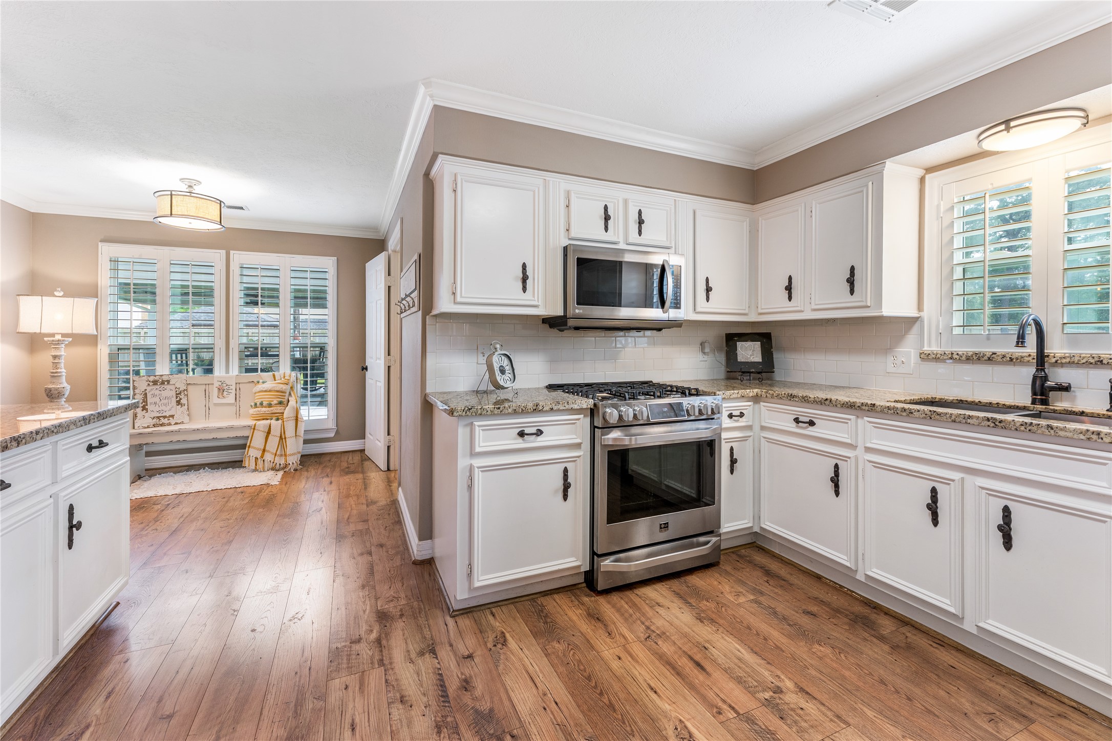 3301 Winter Lane Baytown, TX 77521 - Photo 6 of 28 This inviting kitchen features white cabinetry, granite countertops, and stainless steel appliances. The flooring adds warmth, while large windows with plantation shutters bring in natural light, creating a bright and welcoming space.