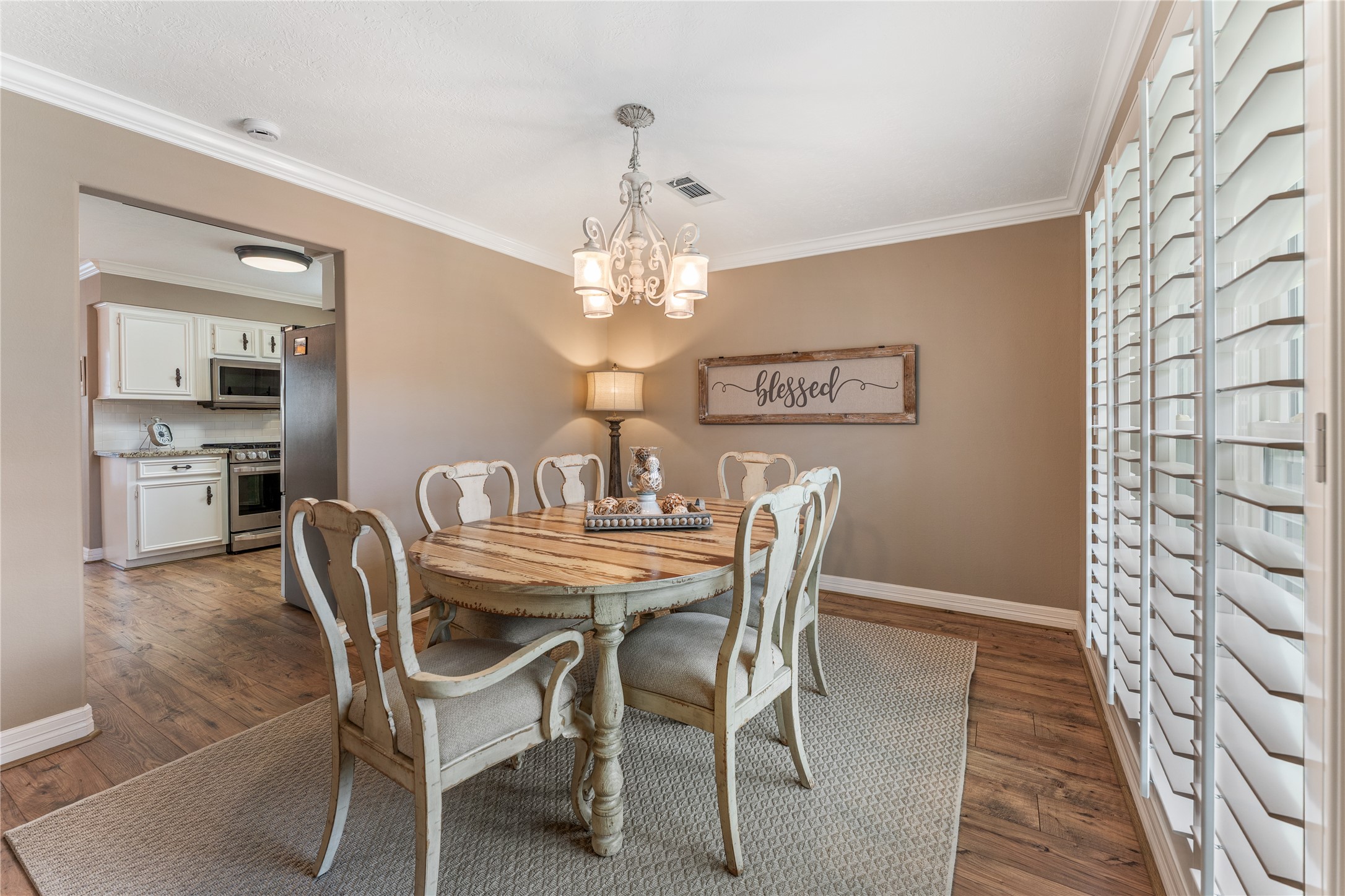 3301 Winter Lane Baytown, TX 77521 - Photo 7 of 28 Natural light streams through large shuttered windows, enhancing the warm, neutral tones of the formal dinning room. The dining space opens into a well-lit kitchen with classic cabinetry and modern appliances.