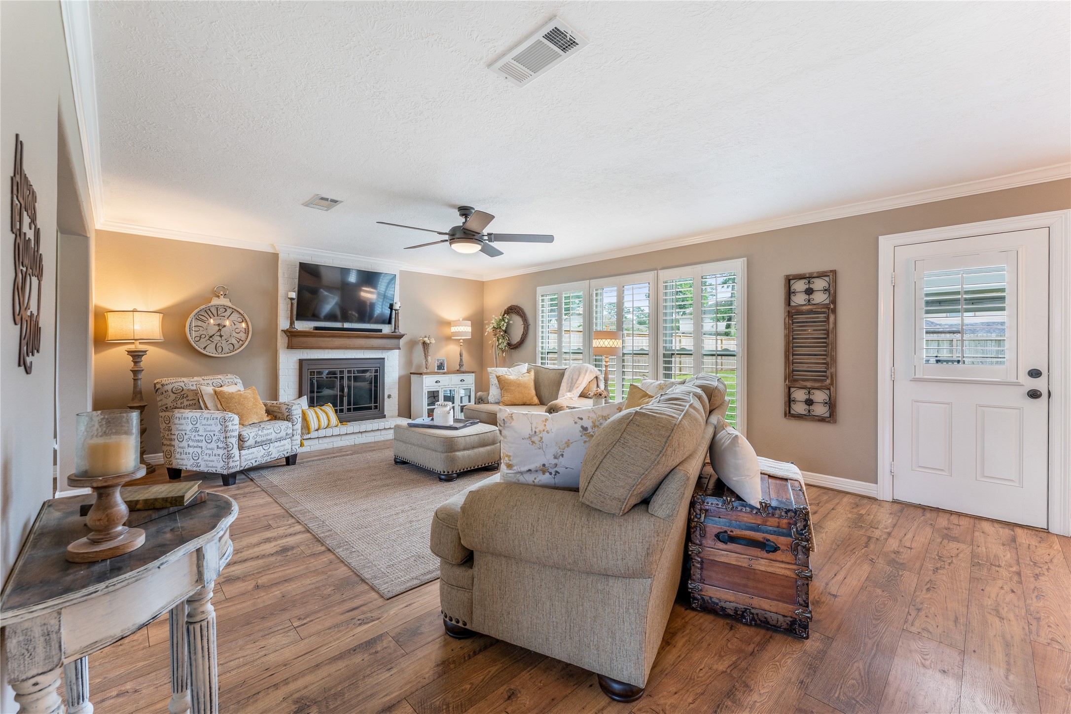 3301 Winter Lane Baytown, TX 77521 - Photo 9 of 28 This inviting Formal living room features a cozy fireplace and abundant natural light through large planation shutter windows. It is tastefully decorated with neutral tones, a ceiling fan, and comfortable seating, creating a warm and welcoming atmosphere.