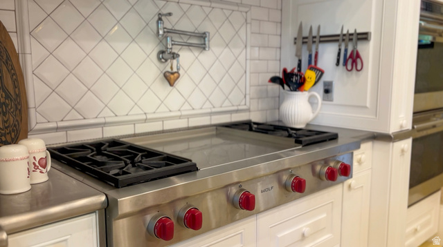426 West Center Street Parowan, UT 84761 - Photo 16 of 107 Professional-grade Wolf range with red control knobs, integrated griddle, stainless steel countertop, white cabinetry with recessed panel doors, and a white subway tile backsplash with a diagonal pattern