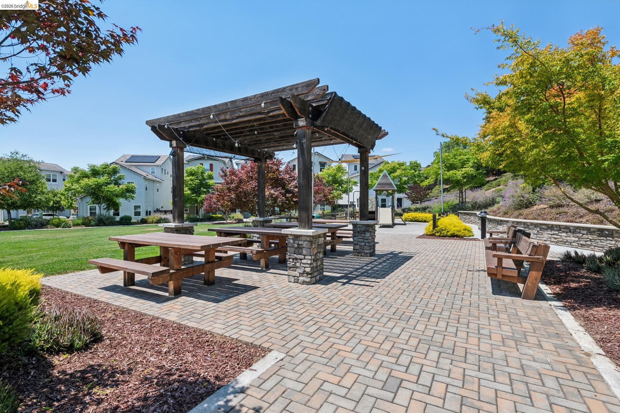 24157 Amaranth Loop Hayward, CA 94541 - Photo 58 of 63 Patio area featuring a wood pergola with string lighting, multiple wooden picnic tables, and stone-clad support columns