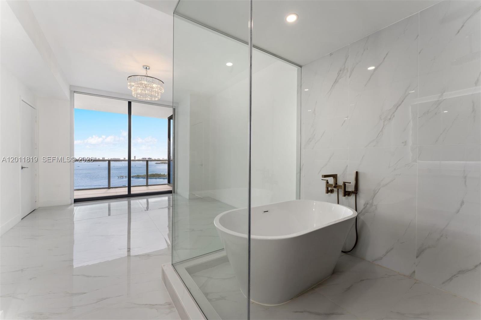 700 Northeast 24th Street, Unit 2504 Miami, FL 33137 - Photo 21 of 52 Spa-inspired primary bathroom featuring dual vanities, a deep soaking tub, a frameless glass rainfall shower, and designer porcelain tile throughout.