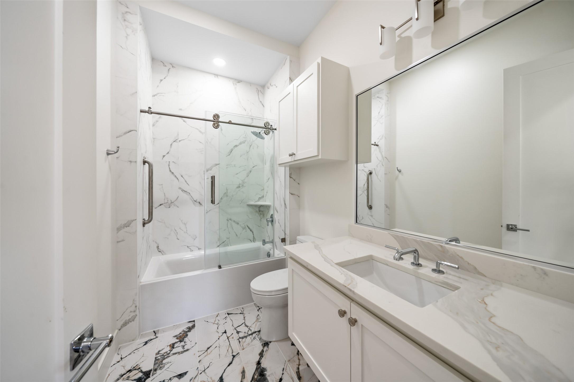 1839 Colquitt Street Houston, TX 77098 - Photo 8 of 19 En-suite bathroom #1 features a modern design with elegant marble-pattern tiles, a glass-enclosed shower-bathtub combo, a sleek vanity with ample storage, and a large mirror with contemporary lighting.