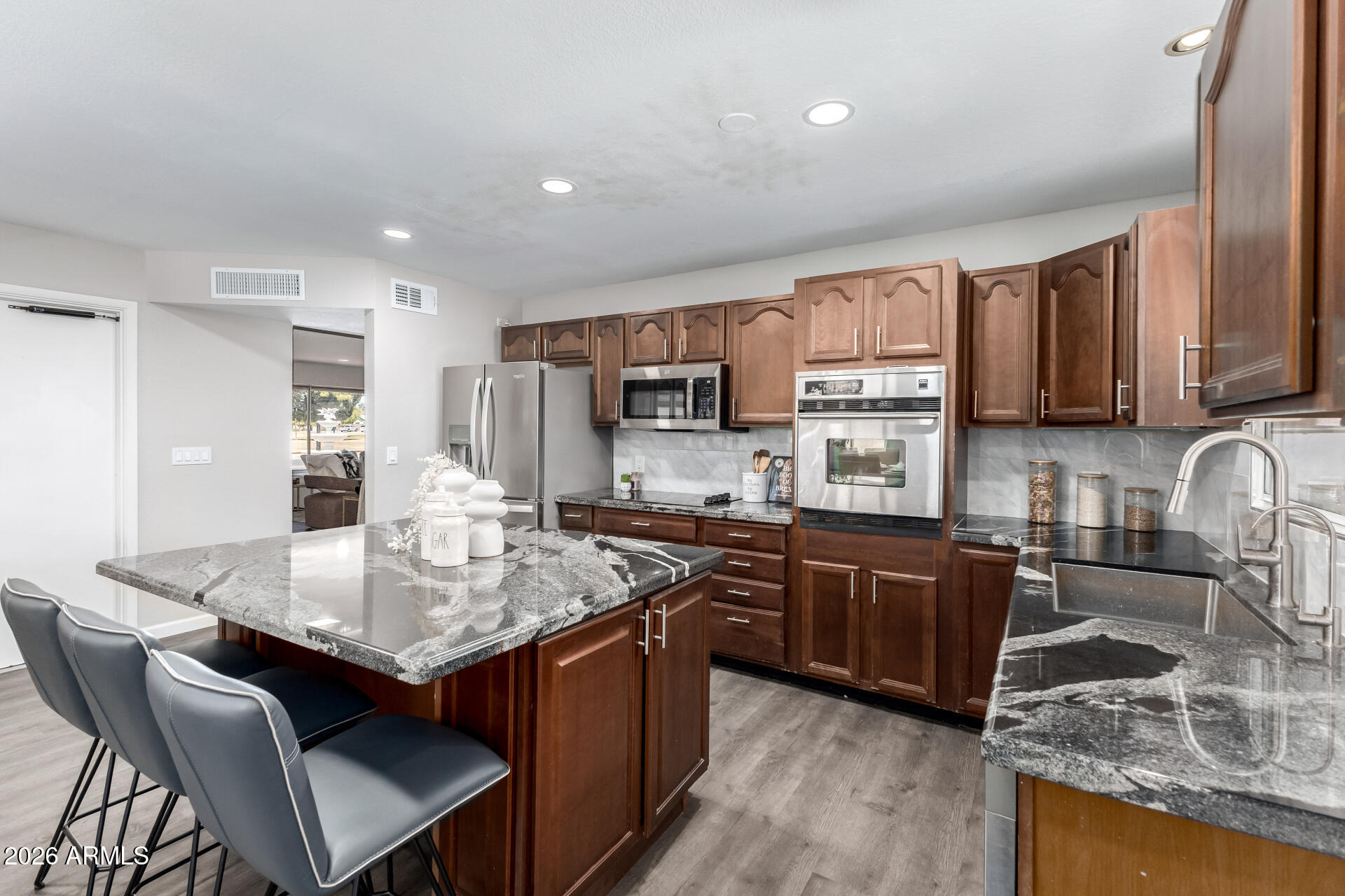 2915 West Hearn Road Phoenix, AZ 85053 - Photo 10 of 28 a kitchen with stainless steel appliances granite countertop a stove top oven a sink dishwasher a dining table and chairs with wooden cabinets