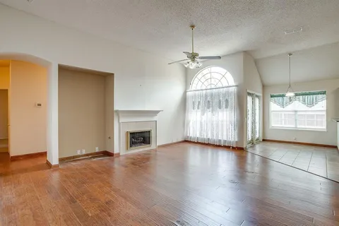 an empty room with wooden floor chandelier and windows