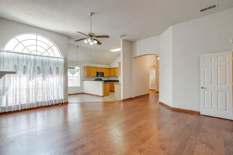 an empty room with wooden floor staircase and windows