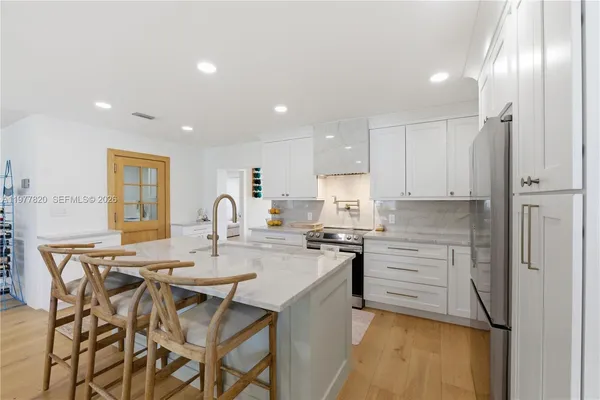a kitchen with stainless steel appliances granite countertop a stove a sink a refrigerator and white cabinets with wooden floor