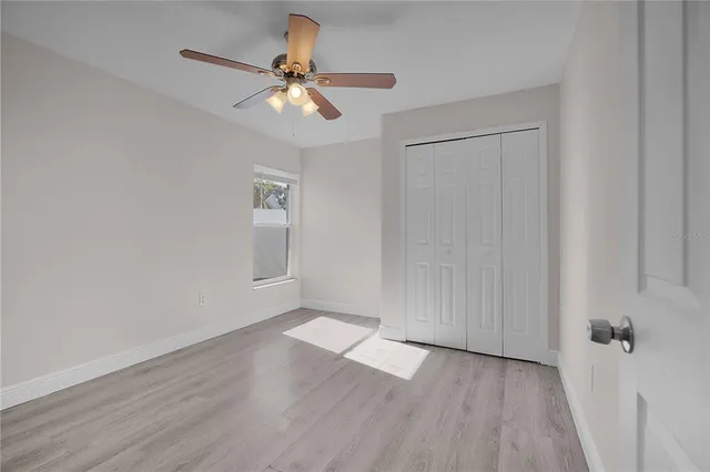 an empty room with wooden floor fan and windows
