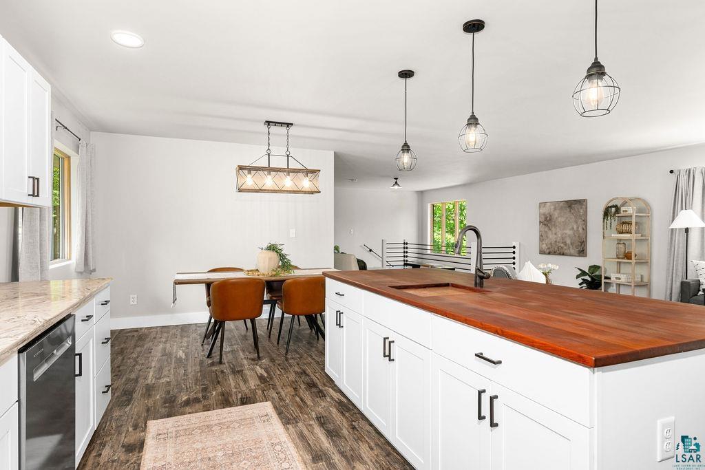 5025 Reid Road Duluth, MN 55803 - Photo 14 of 51 Open-concept kitchen and dining area featuring a large center island with a wood-finish countertop, white cabinetry with black hardware, wood-finish flooring, and pendant lighting
