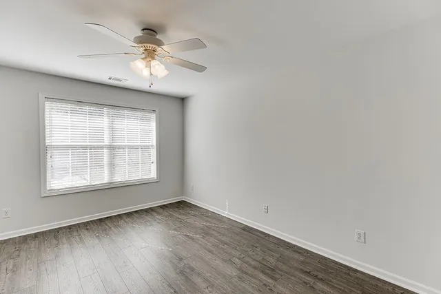 an empty room with wooden floor fan and windows