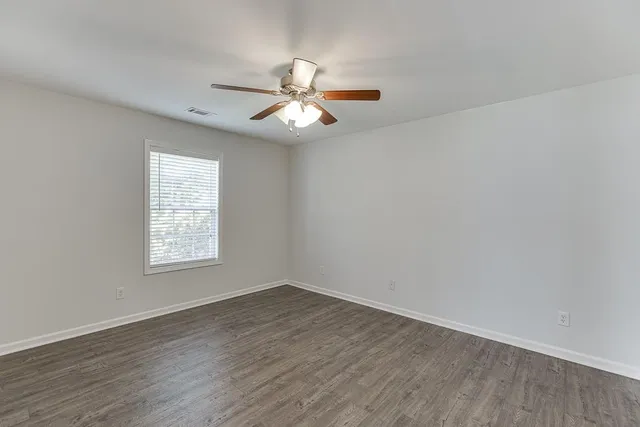 an empty room with wooden floor fan and windows