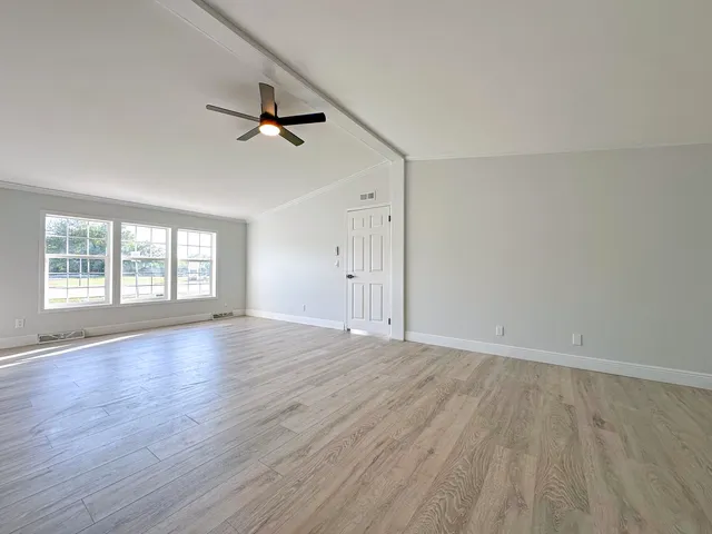an empty room with wooden floor ceiling fan and windows