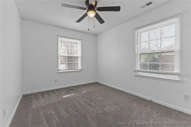 an empty room with chandelier fan and windows
