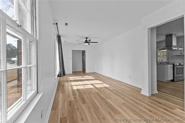 a view of empty room with wooden floor and kitchen
