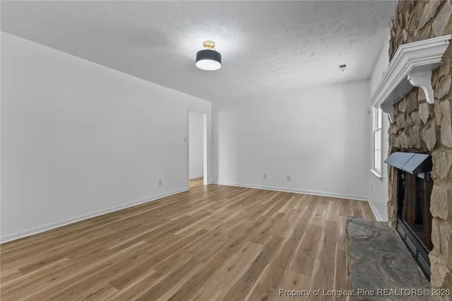 a view of an empty room with wooden floor and a fireplace