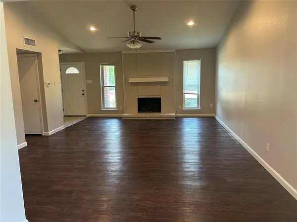 an empty room with wooden floor fireplace and windows