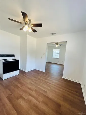 a view of an empty room with wooden floor and a ceiling fan
