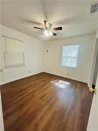 an empty room with wooden floor ceiling fan and windows