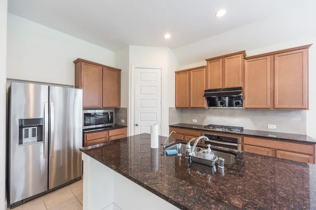 a kitchen with stainless steel appliances granite countertop a refrigerator a stove and a sink with wooden floor