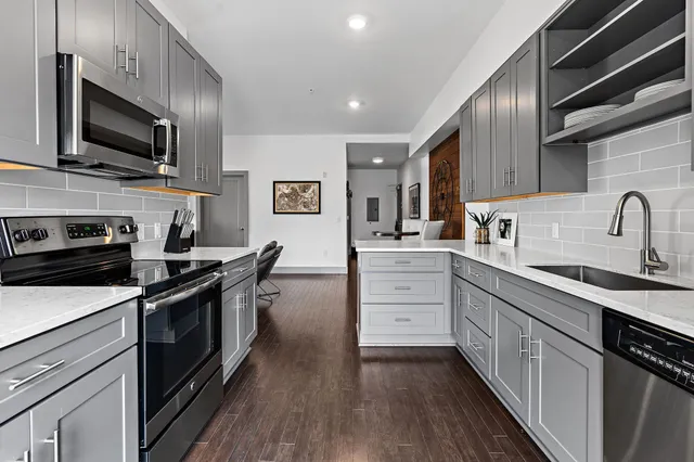 a kitchen with stainless steel appliances a sink dishwasher a stove top oven a refrigerator with wooden floor and cabinets