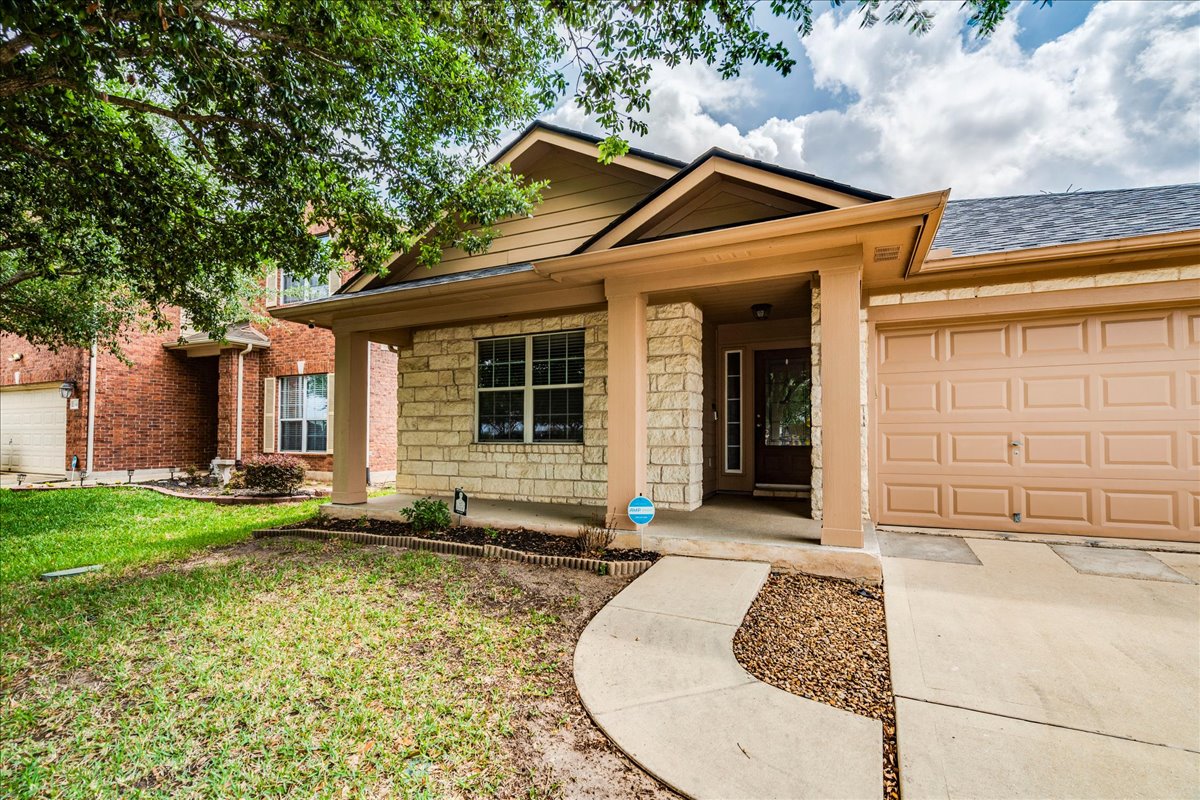 1151 Stone Rim Loop Buda, TX 78610 - Photo 2 of 35 The property features a stone and siding exterior, a covered porch entryway, and an attached garage with a panel door