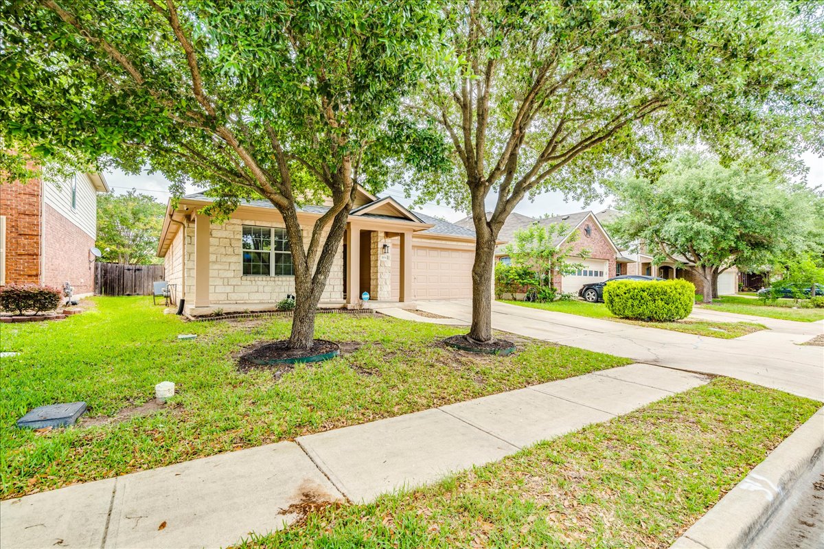 1151 Stone Rim Loop Buda, TX 78610 - Photo 33 of 35 The property features a stone and stucco exterior, a well-maintained lawn, and mature trees in the front yard