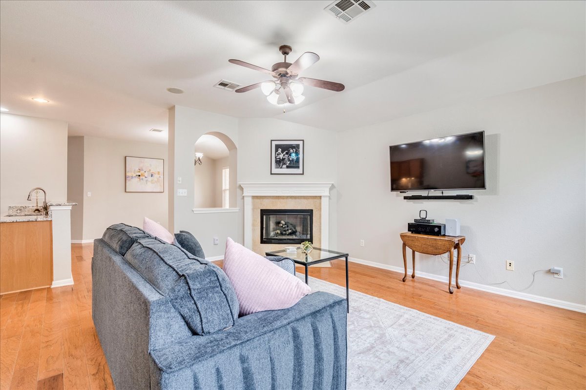 1151 Stone Rim Loop Buda, TX 78610 - Photo 5 of 35 The living area features hardwood floors, a ceiling fan, and a fireplace with a light-colored mantel