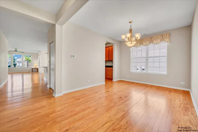 an empty room with wooden floor chandelier and windows