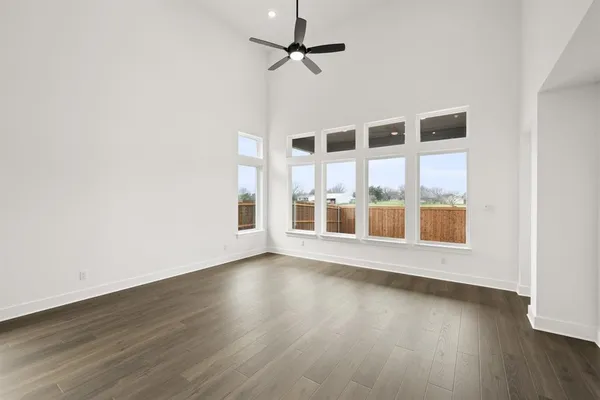 an empty room with wooden floor fan and windows