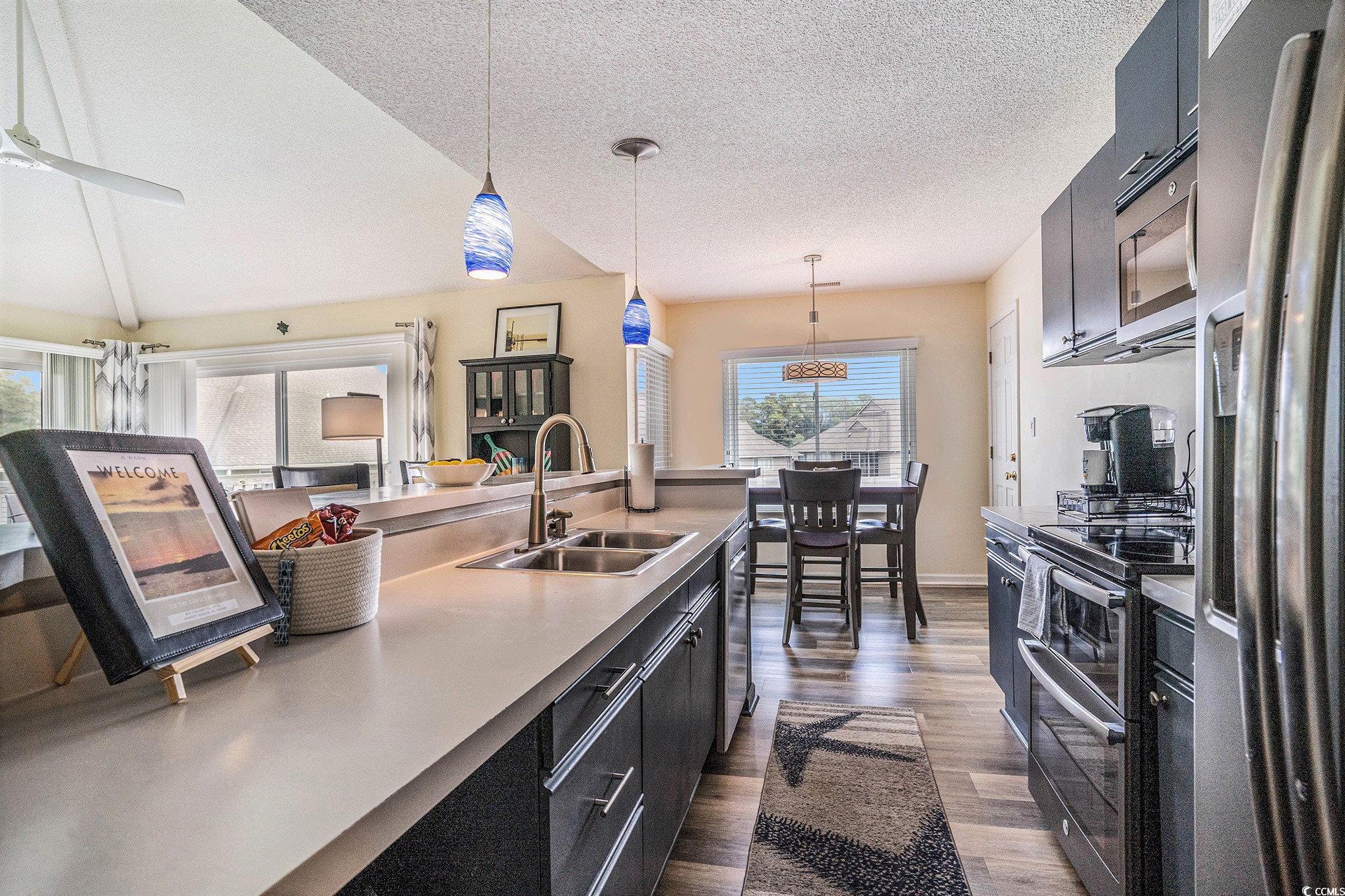 815 Colony Place, Unit 15F Sunset Beach, NC 28468 - Photo 7 of 34 Kitchen featuring dark cabinets, decorative light fixtures, appliances with stainless steel finishes, dark wood-style floors, and a textured ceiling