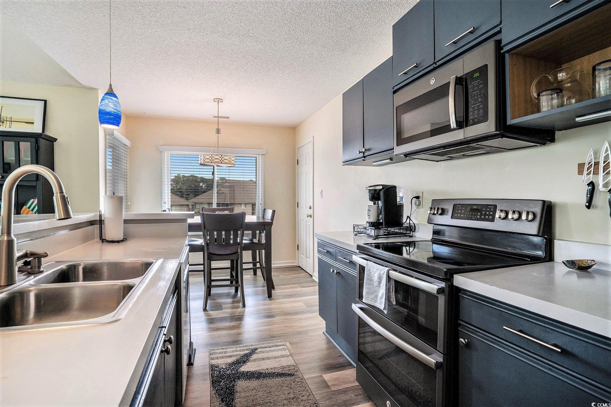 815 Colony Place, Unit 15F Sunset Beach, NC 28468 - Photo 8 of 34 Kitchen with stainless steel appliances, hanging light fixtures, dark cabinets, a textured ceiling, and dark wood finished floors