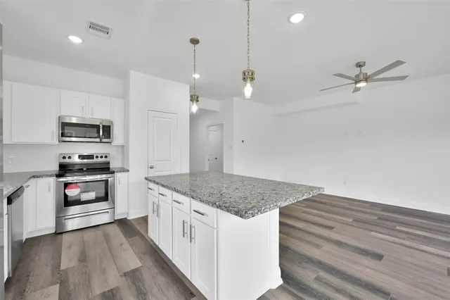 a kitchen with stainless steel appliances granite countertop a refrigerator a sink dishwasher a stove and white cabinets with wooden floor