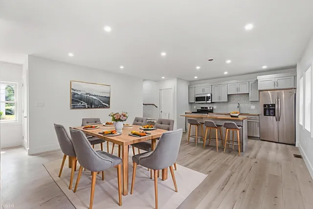 a dining room with stainless steel appliances kitchen island granite countertop a dining table chairs and a refrigerator