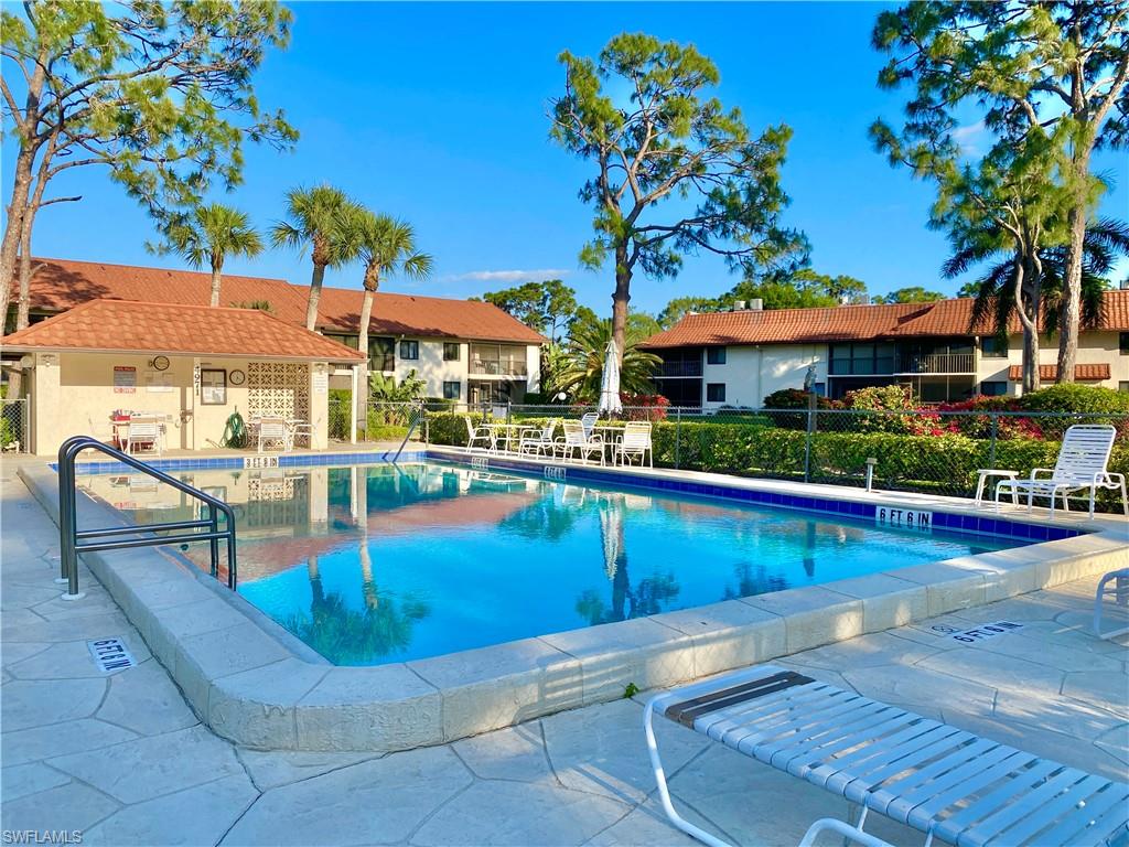 4955 Pepper Circle, Unit B204 Naples, FL 34113 - Photo 20 of 25 a view of a swimming pool with a table and chairs under an umbrella