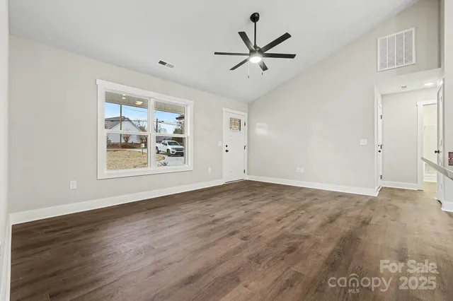 a view of an empty room with wooden floor and a ceiling fan
