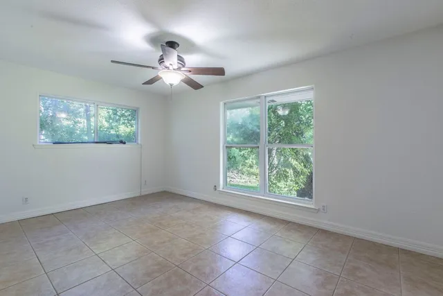 a view of an empty room with windows and chandelier fan