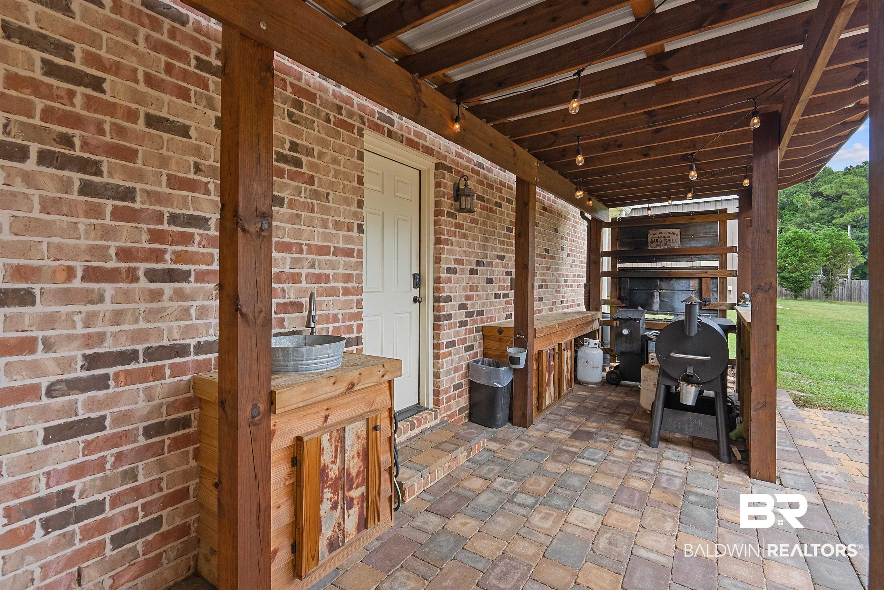 12070 Comalander Road Fairhope, AL 36532 - Photo 43 of 50 Covered patio featuring a brick exterior wall, wood beam supports, string lighting, and a paved stone floor