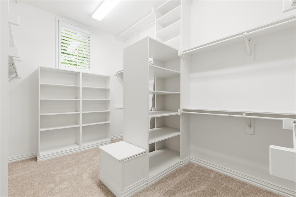 967 East Bethel School Road Coppell, TX 75019 - Photo 28 of 39 Walk-in closet featuring extensive built-in shelving, multiple hanging rods, a central storage unit with a seating area, and a window with plantation shutters