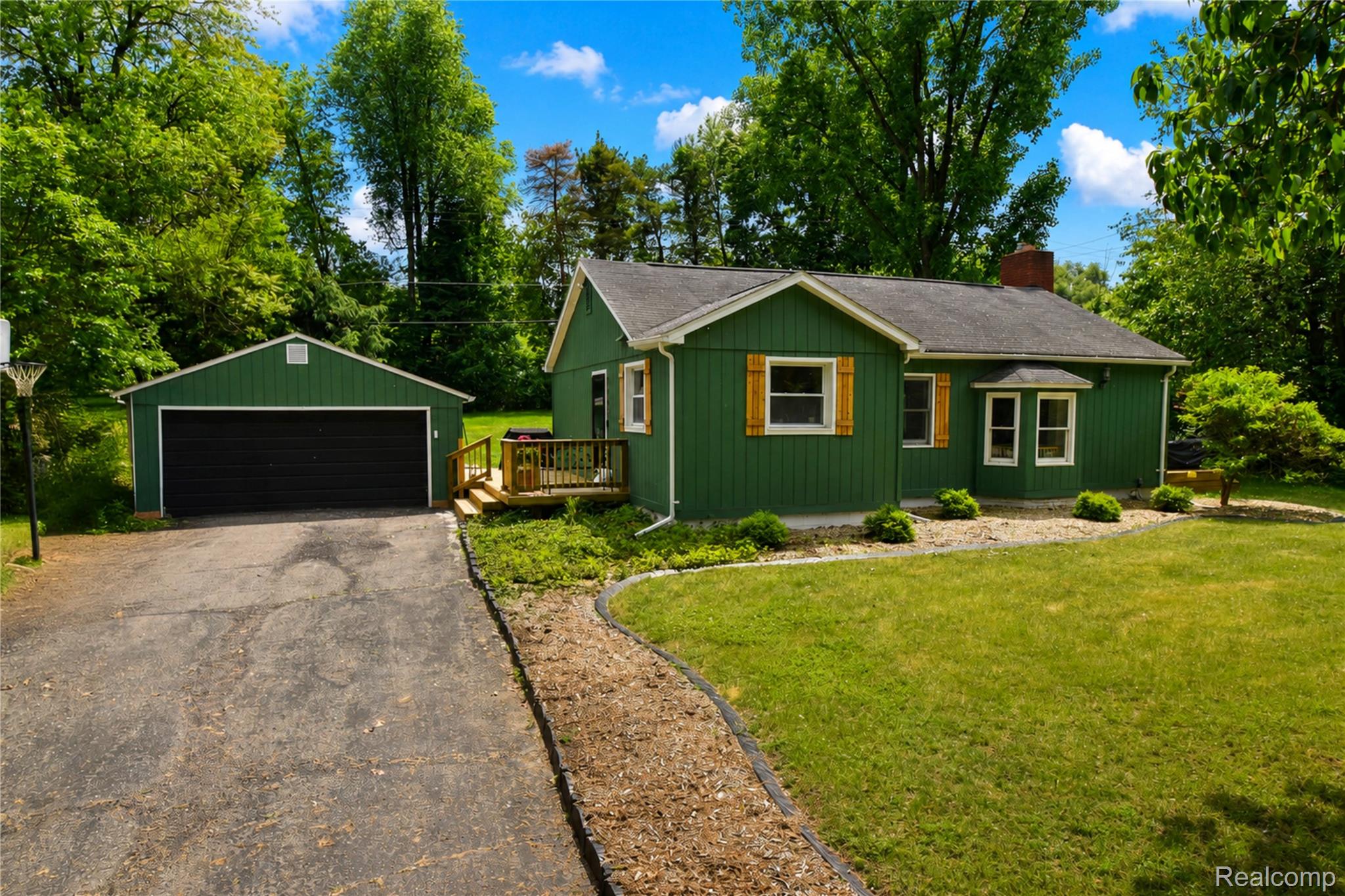1405 Middle Road Highland, MI 48357 - Photo 1 of 18 Green ranch-style home featuring a detached two-car garage, asphalt driveway, front lawn, and mature trees