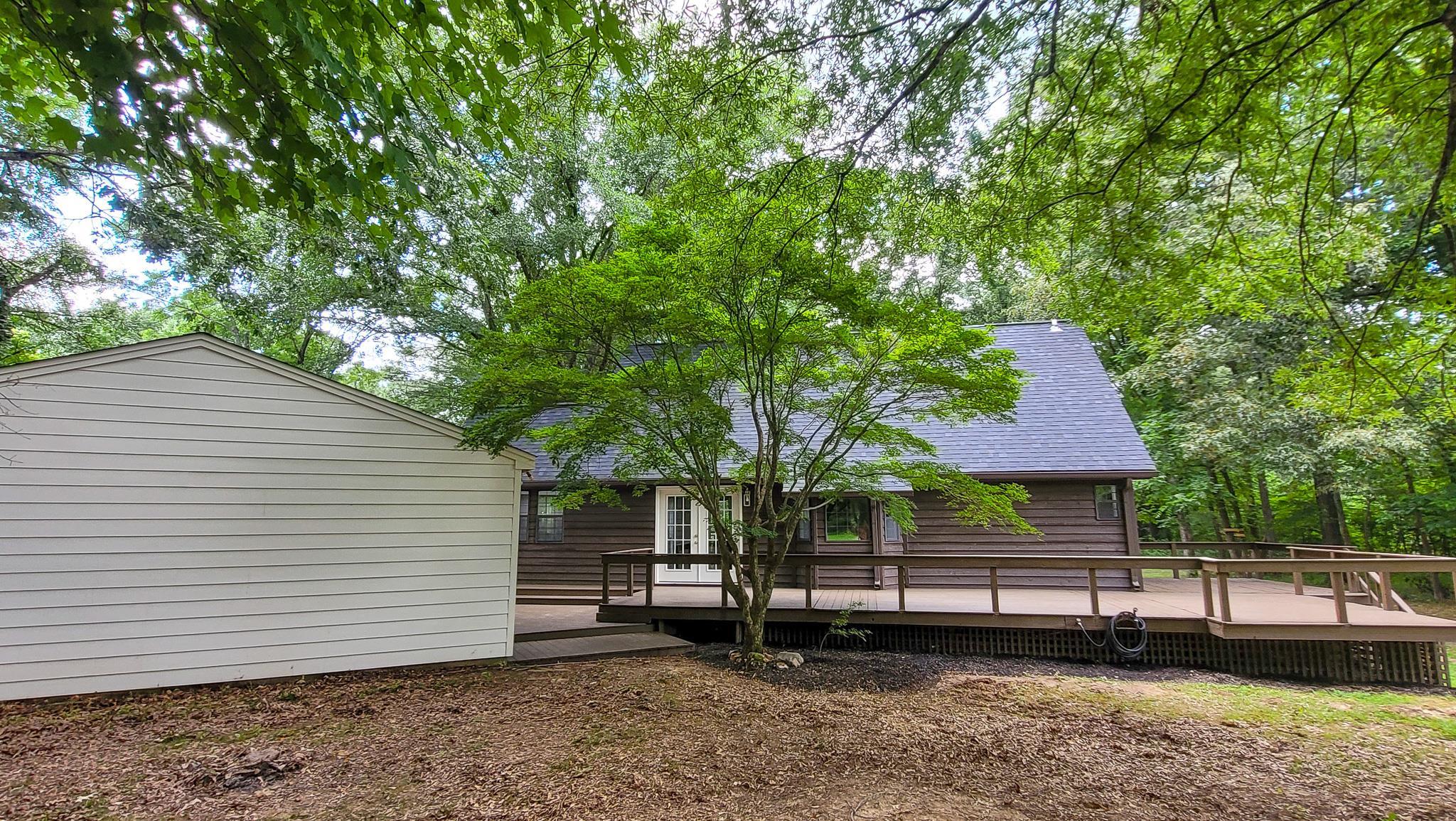 470 Rich Road Somerville, TN 38068 - Photo 8 of 40 Expansive wood-finish deck with railings, set against a dark-paneled exterior and a new dark shingle roof