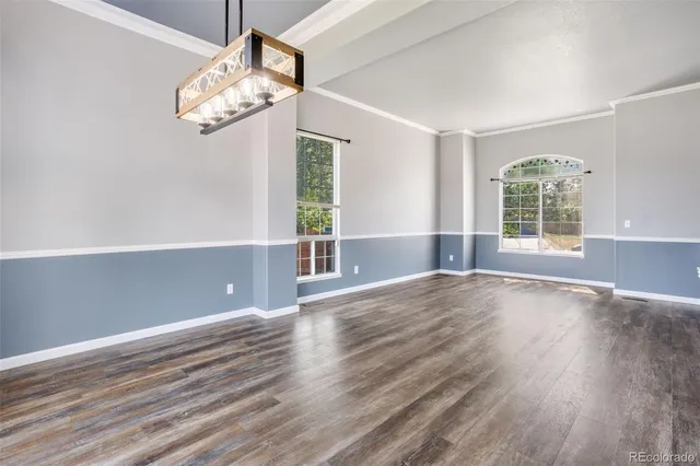 an empty room with wooden floor chandelier and windows