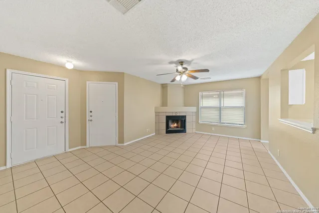 a view of an empty room with chandelier fan and fire place