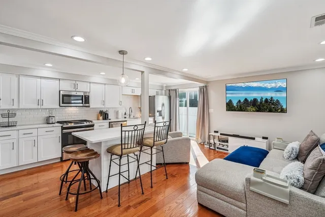 a living room with stainless steel appliances kitchen island granite countertop a stove a sink a dining table and chairs with wooden floor