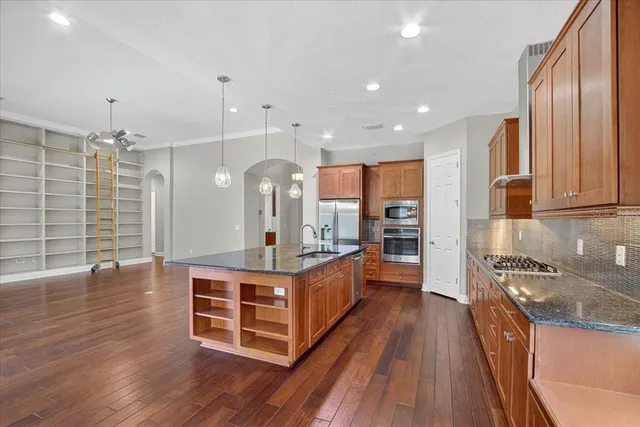 a large kitchen with stainless steel appliances a large counter top a stove and a wooden floors