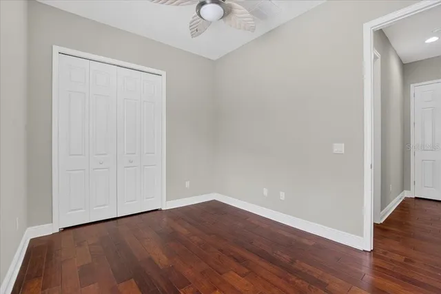 a view of an empty room with wooden floor and a ceiling fan