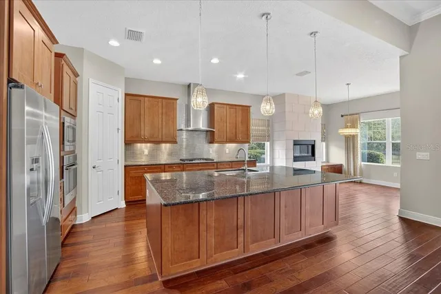 a large kitchen with stainless steel appliances kitchen island granite countertop wooden floors and view of living room