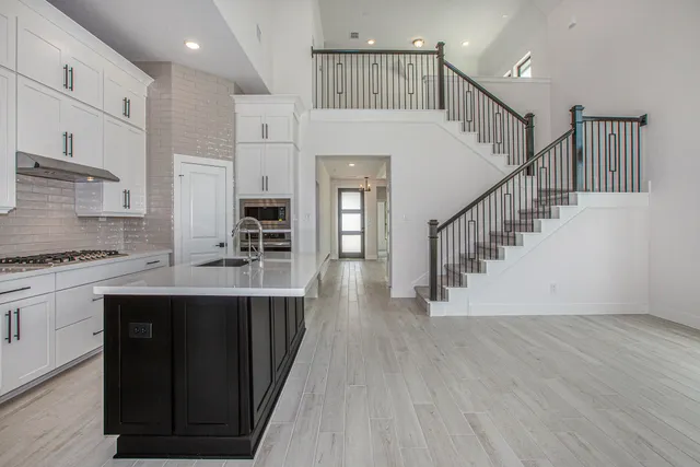 a kitchen with stainless steel appliances granite countertop a refrigerator oven a sink dishwasher and white cabinets with wooden floor