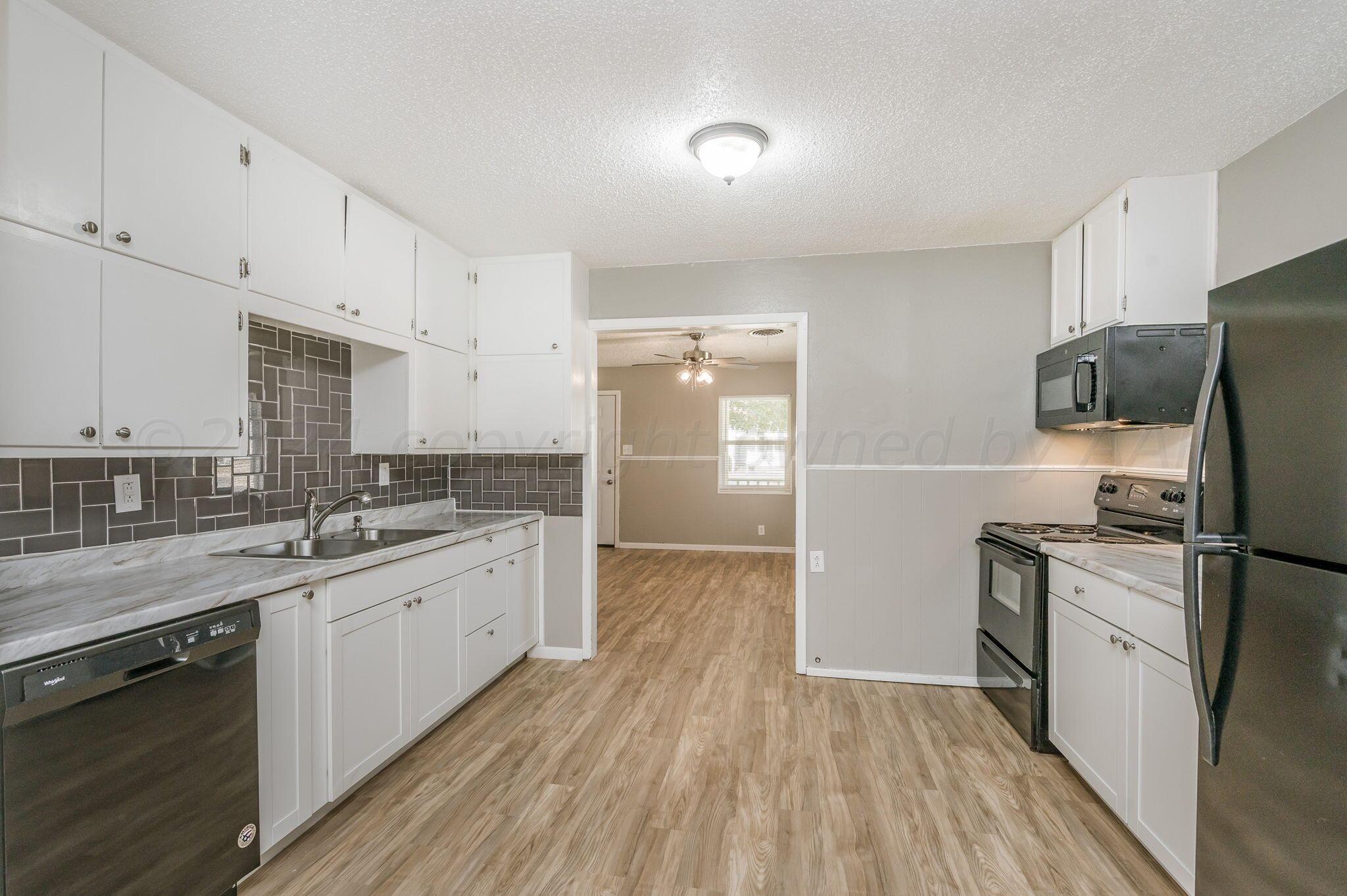 4207 South Ong Street Amarillo, TX 79110 - Photo 5 of 16 a kitchen with a sink a refrigerator and white cabinets