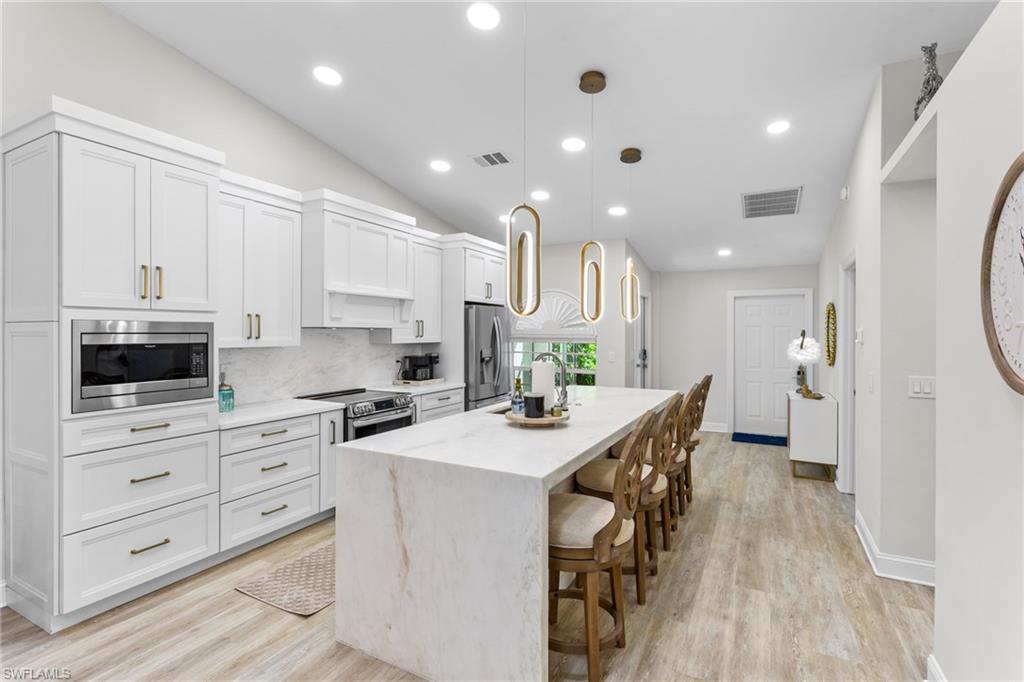 754 Wiggins Bay Drive Naples, FL 34110 - Photo 3 of 34 a kitchen with stainless steel appliances kitchen island granite countertop a stove a sink a refrigerator and white cabinets with wooden floor