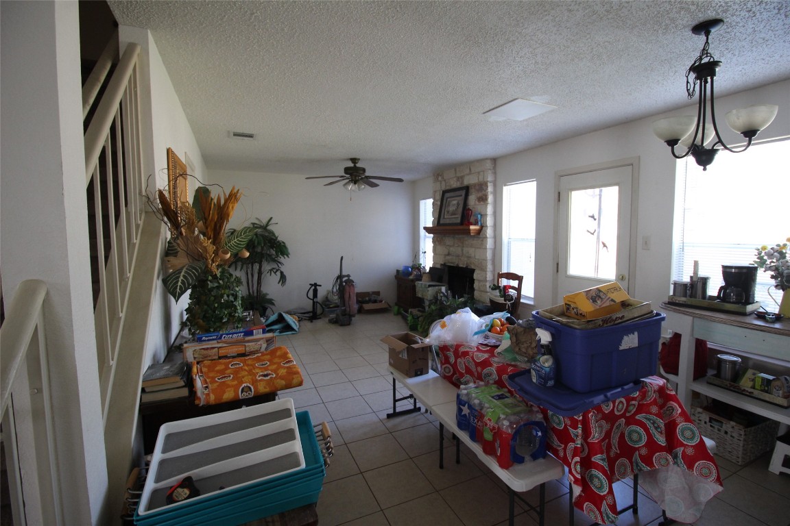 808 Angleton Cove Austin, TX 78748 - Photo 5 of 17 Dining room featuring a stone fireplace, light tile patterned floors, a chandelier, a textured ceiling, and a ceiling fan